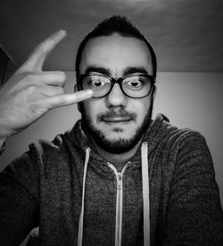 Close-up portrait of man gesturing horn sign against wall