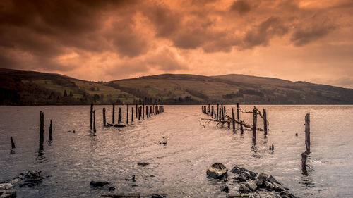 Wooden posts in lake against sky