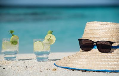 Close-up of drinks by straw hat and sunglasses at beach