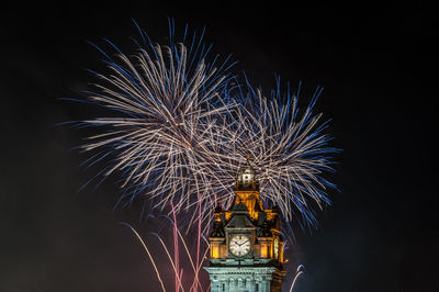 Low angle view of illuminated clock tower and firework display at night