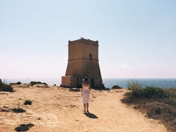 Rear view full length of woman standing against ghajn tuffieha tower