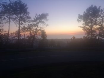 Silhouette trees by road against sky during sunset