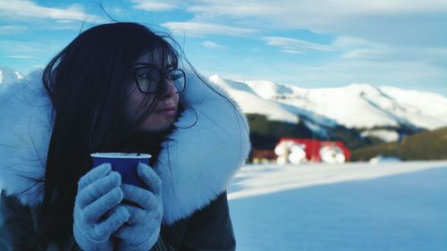 Close-up of woman in fur coat holding coffee against sky during winter