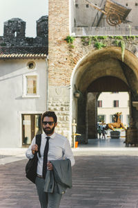 Businessman holding blazer while walking on city street