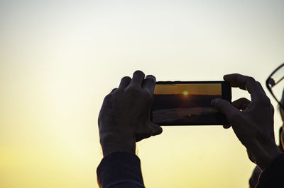 Midsection of man photographing against sky during sunset