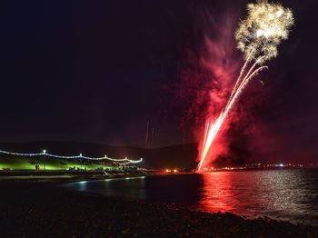 Firework display over sea against sky at night