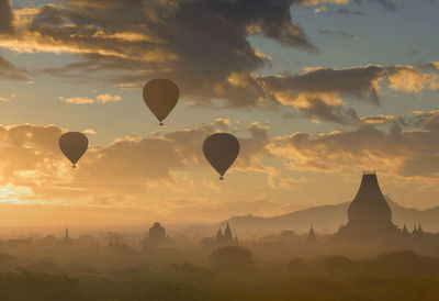 Hot air balloons flying over landscape against sky during sunset