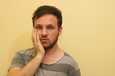 Close-up portrait of young man touching cheek against wall