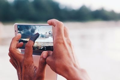 Cropped hands photographing sea through mobile phone