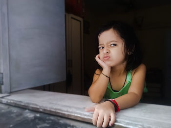 Portrait of cute girl making face while sitting by window