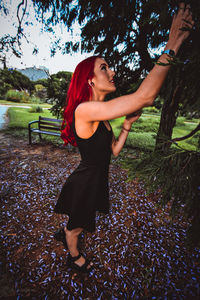 Side view of young woman standing against trees