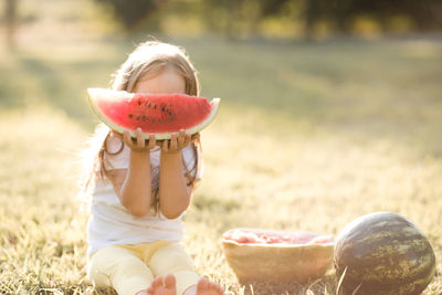 Cute girl holding watermelon sitting at park