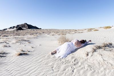 Woman lying on sand at beach against clear sky