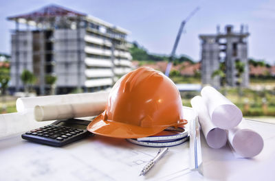 Close-up of blueprints with helmet and calculator on table against building