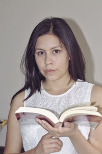 Portrait of woman holding book against wall