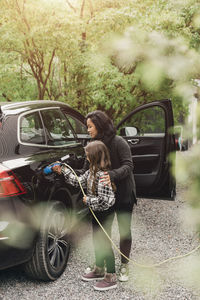 Mid adult woman teaching daughter to charge electric car at charging station