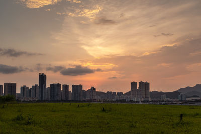Scenic view of field and buildings against sky during sunset
