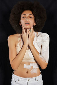 Portrait of beautiful young woman with paint against black background