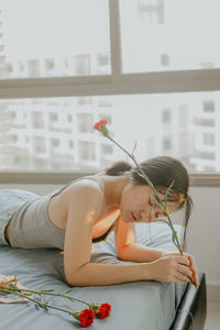 Woman holding flower while lying on bed at home