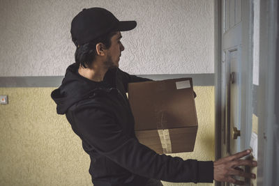 Side view of delivery man with package ringing bell at doorstep