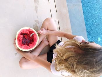 High angle view of mid adult woman having watermelon while sitting at poolside