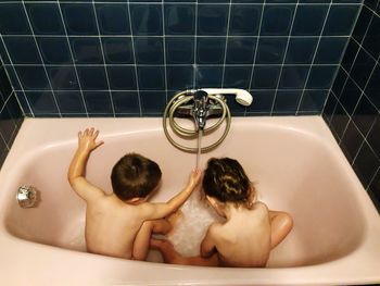 High angle view of naked siblings sitting in bathtub