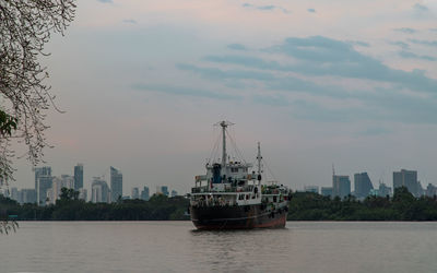 Nautical vessel on sea by buildings in city against sky