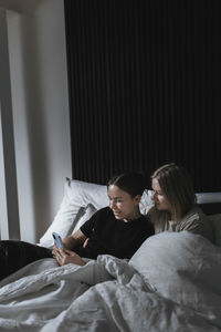 Female homosexual couple sitting in bed and looking at cell phone