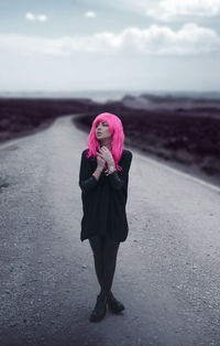 Young woman with dyed hair standing on road against sky