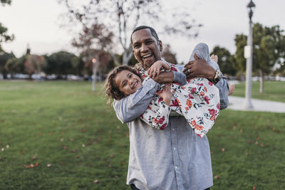 Happy father holding cute girl at park playground at dusk