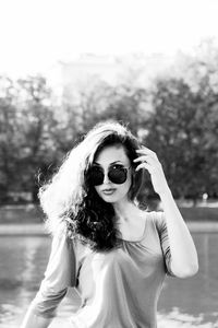 Portrait of woman wearing sunglasses against lake and trees
