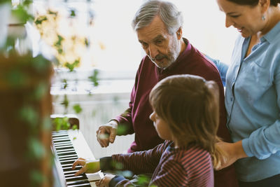 Mother and great grandfather looking at boy playing piano in house