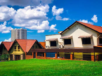 Houses by lawn and buildings against sky