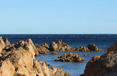 Scenic view of rocks in sea against clear blue sky