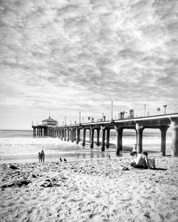 People on beach by bridge against sky