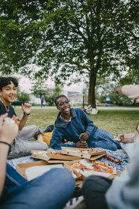 Happy teenage boys enjoying with friends while sitting and eating pizza in park
