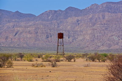 Water tower on field against rocky mountains