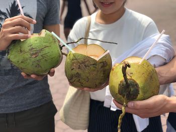 Midsection of friends holding coconuts while standing at beach