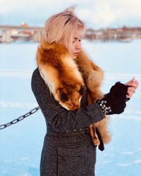 Young woman wearing worm clothing while standing against sky