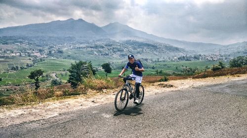 Man riding bicycle on road against mountains