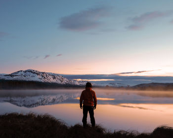 Rear view of man standing on mountain against sky during sunset