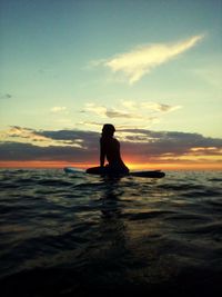 Silhouette man in sea against sky during sunset