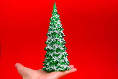 Woman hand holding green christmas tree toy isolated on red background