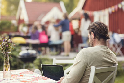 Rear view of man using laptop while sitting on chair in back yard