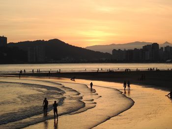 Silhouette people on beach against sky during sunset