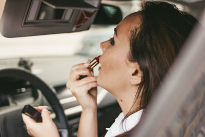 Woman applying lipstick in car