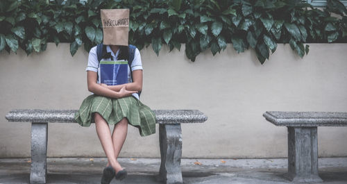 Schoolgirl wearing paper bag with insecurities text while sitting on stone bench