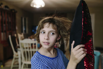 Close-up of girl with short hair holding cushion while standing at home