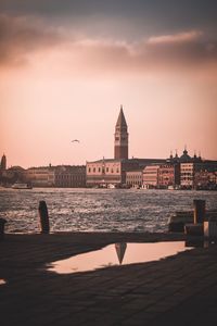 Buildings at waterfront against cloudy sky