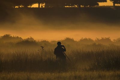 Man standing on field against sky during sunset